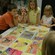 A woman talks to kids who are gathered around colorful illustrations on a table